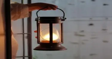 holding the curved iron handle of a lantern with one hand, the lantern is hanging slightly, not touching the glass