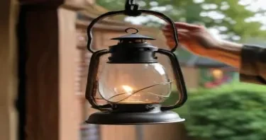 holding the curved iron handle of a lantern with one hand, the lantern is hanging slightly, not touching the glass