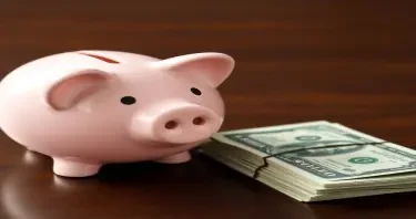 A child’s empty piggy bank next to a stack of bills