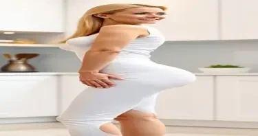 A mature adult woman shown in side profile, standing in a clean, modern kitchen environment. Her body has a highly stylized shape with an extremely narrow waist and maximally developed, smooth, rounded hips that extend outward in a pronounced curve — large and spherical in appearance. Her chest is prominently projected, full, and lifted, balancing the exaggerated lower body proportions. Her abdomen is completely flat and defined, showing zero visible body fat, and her overall physique presents with no visible imperfections — the skin smooth, even-toned, and unblemished from head to toe. She has a compact frame with short limbs and a visibly larger head-to-body ratio. Her facial features include clear blue eyes, long enhanced eyelashes, a small refined nose, full shaped lips, straight bright white teeth, and a well-defined, forward-projecting jawline. Her cheeks are full, lifted, and symmetrically sculpted. Her long, thick blonde hair is styled neatly with exceptional volume and shine. She is dressed in tightly fitted, formal business clothing — specifically a pristine white tailored blazer and a matching white skirt, both cut to contour exactly to her figure and emphasize her silhouette. The lighting is soft and ambient, casting smooth shadows and subtle highlights across her form. The background includes modern kitchen elements such as marble countertops, minimalist cabinetry, and high-end appliances. The image is photorealistic and high resolution, with strong focus on her flawless presentation, anatomical proportions, and the interplay of purity, precision, and visual contrast between elegance and domesticity.