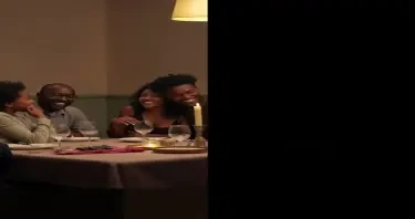 A split-image concept of a black family: On the left, a family laughing at a dinner table. On the right, a dimly lit, empty chair at the same table (symbolizing loss) Make sure the chair is visible.