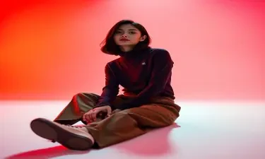 wide and low angle, cinematic, fashion photography for the brand Uniqlo. Woman sitting on floor wearing a Uniqlo heattech top, and brown chinos. The background is a gradient, red, pink and orange